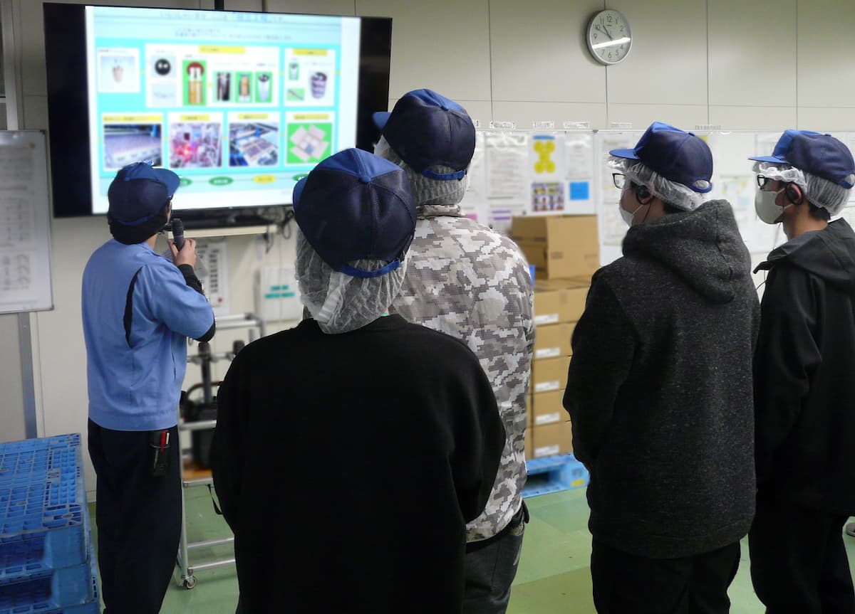 製造工程内で製造の流れの説明を受ける様子